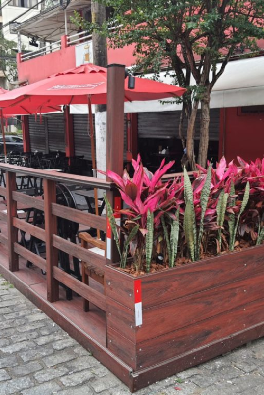 Restaurante com cerca de madeira e guarda-sóis vermelhos, criando um ambiente acolhedor e convidativo ao ar livre.