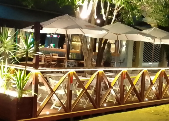 Restaurante à noite, com mesas e guarda-sóis iluminados, criando um ambiente acolhedor e convidativo.